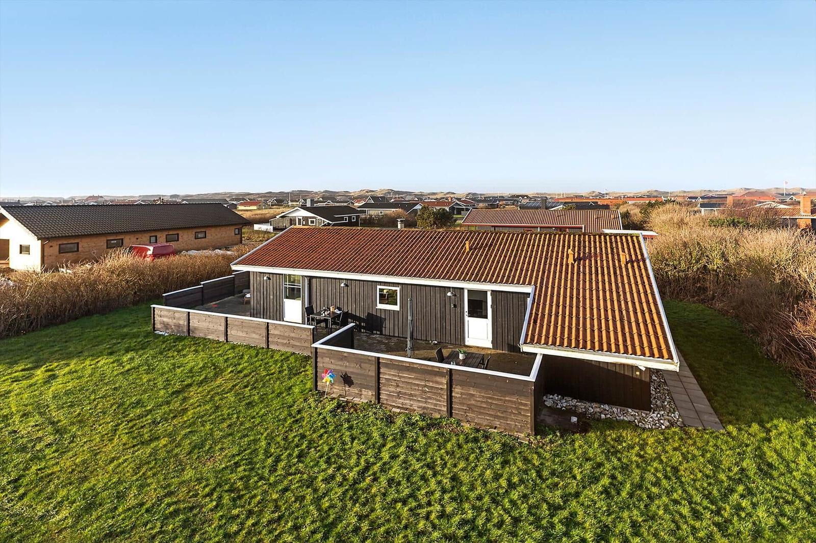 Ein Haus mit Holzfassade und rotem Dach auf grünem Grundstück mit Terrasse.