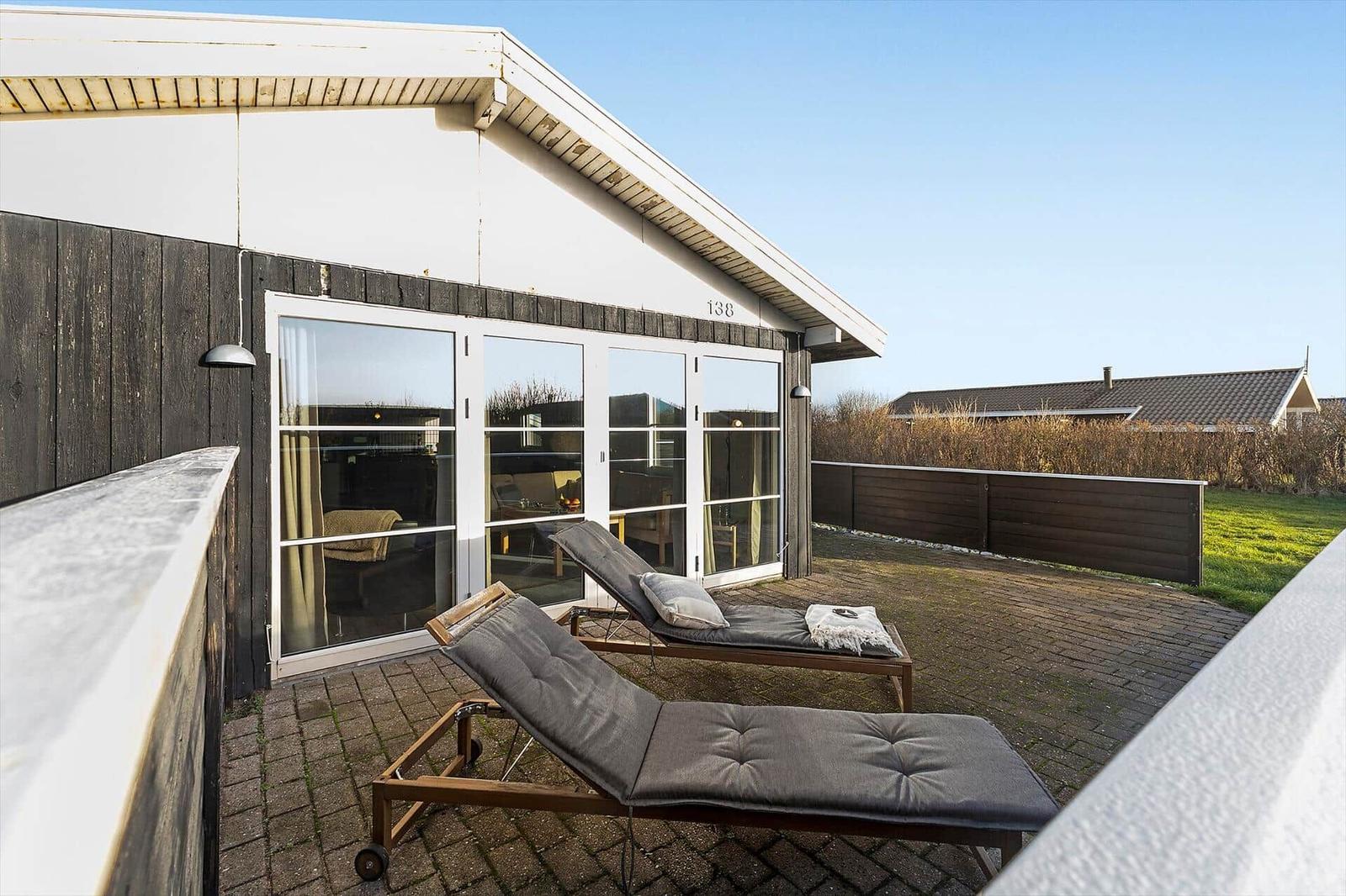Terrasse mit zwei Liegestühlen vor einem Haus mit Glasfront und dunkler Holzfassade.