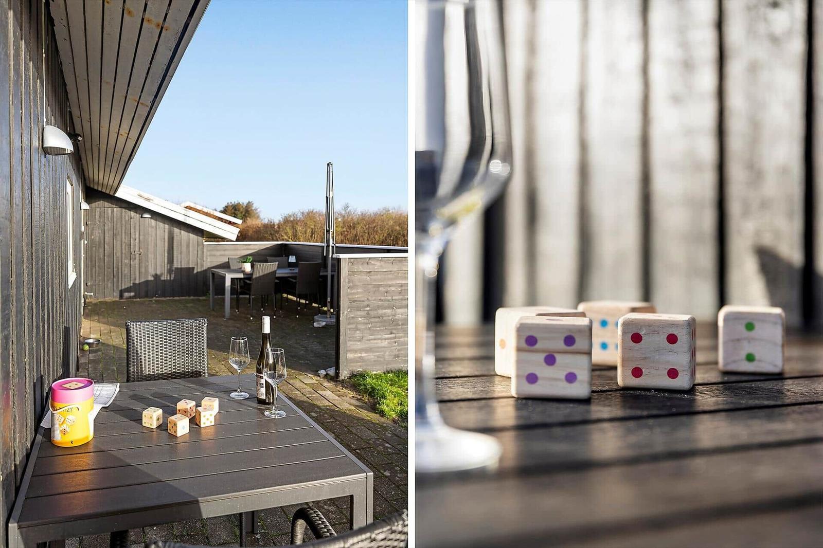 Terrasse mit Tisch, Stühlen und Würfeln. Im Hintergrund ein Grillbereich.