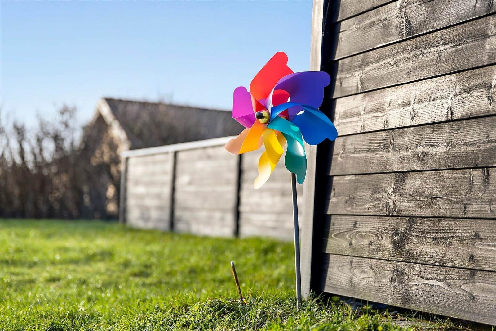 Farbenfroter Windrad steht im Garten neben einer Holzwand.