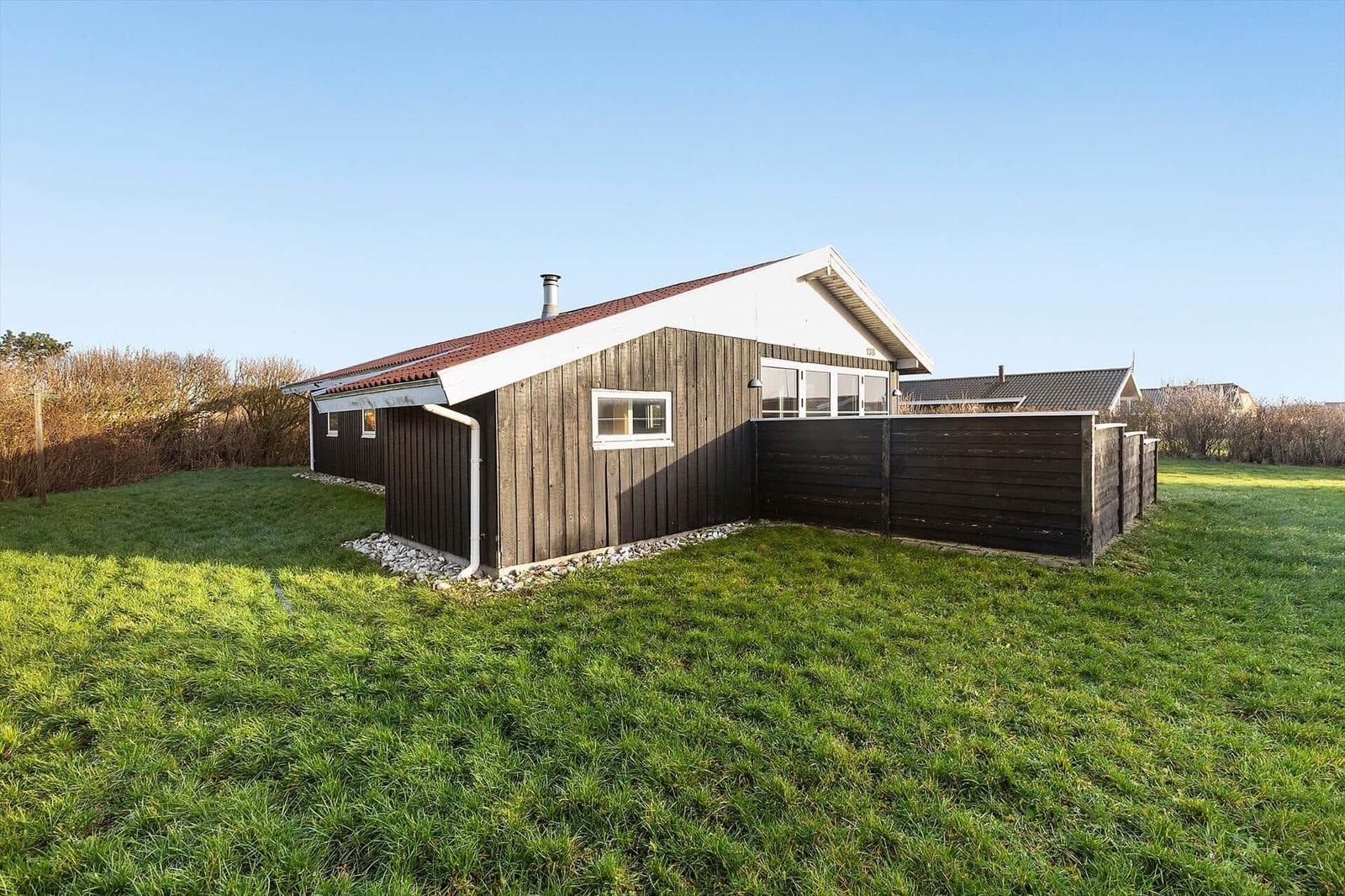 Ein Haus mit dunklem Holzverkleidung und rotem Dach, umgeben von Gras und Hecken.