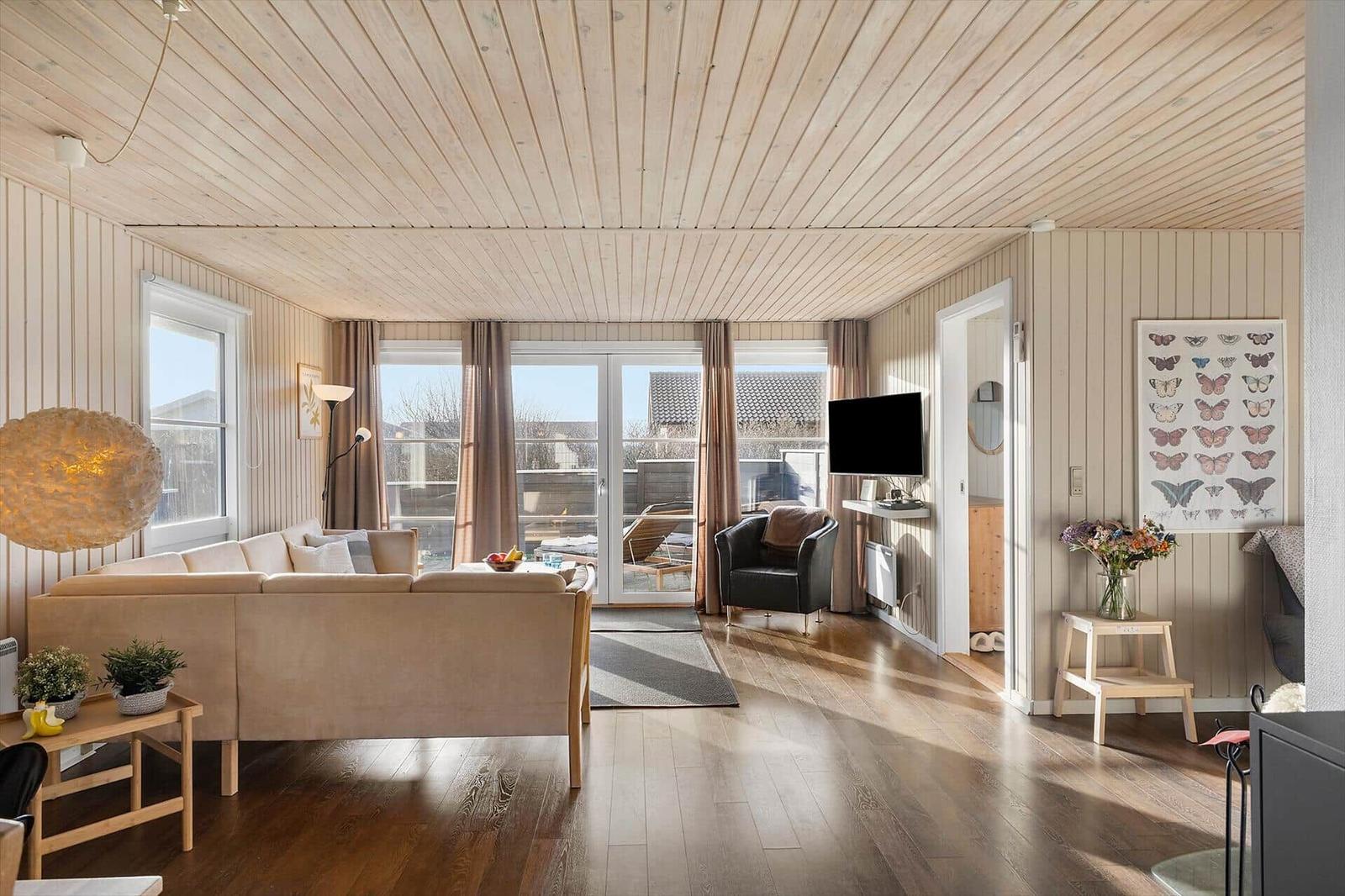 Wohnzimmer mit Holzdecke, Sofa, Fernseher und Blick auf Balkon.