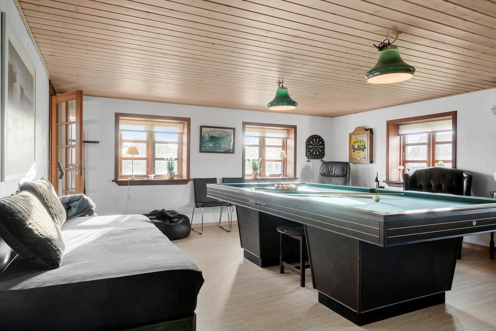 Room with pool table, sofa, windows, and ceiling lights.