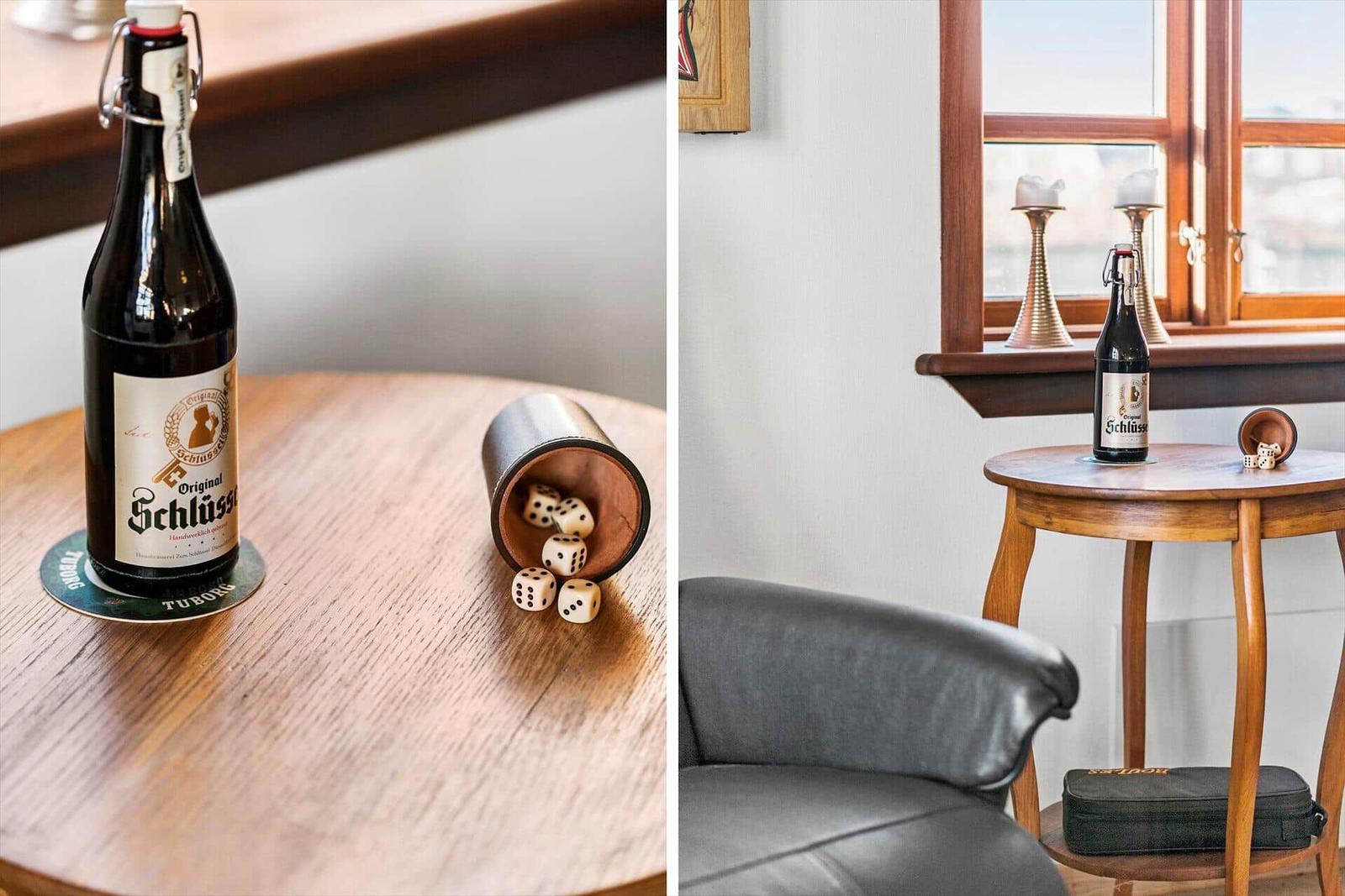 A table with a beer bottle and dice next to a window and a chair.