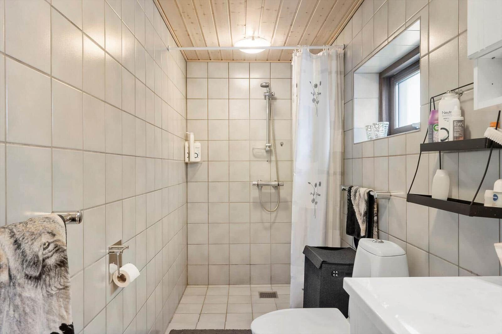 Bathroom with shower, toilet, and sink. White tiles and wooden ceiling.
