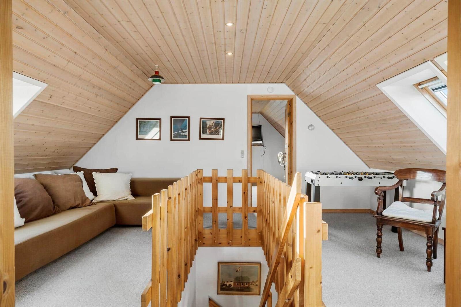 Attic room with sofa, foosball table, and wooden railing.