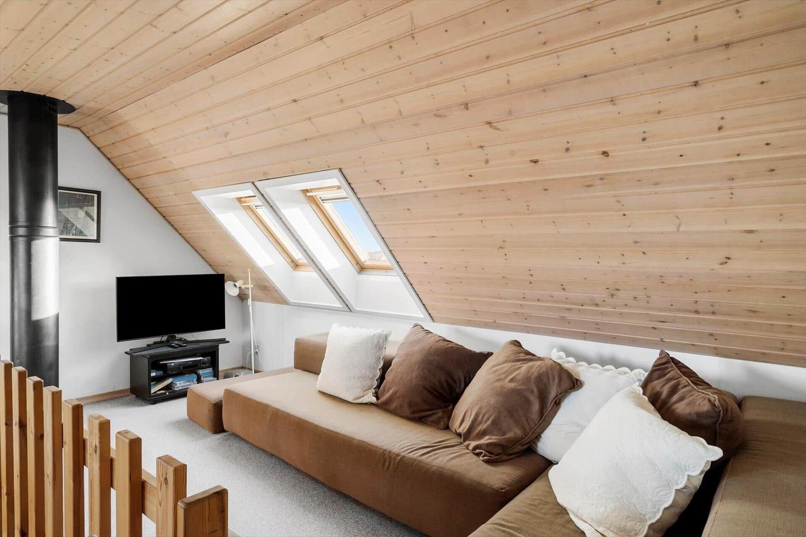 Living room with sofa, TV, and skylights under wooden ceiling.