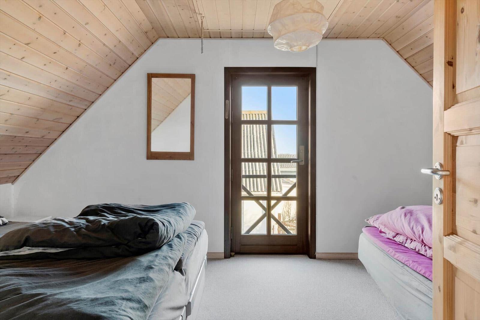 Two beds under wooden ceiling, glass door, mirror, and ceiling light.