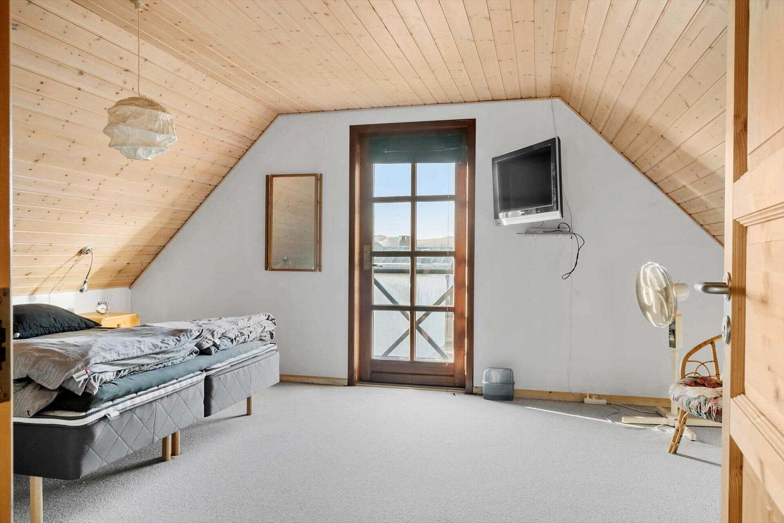 Bedroom with wooden ceiling, bed, TV, and door to balcony.