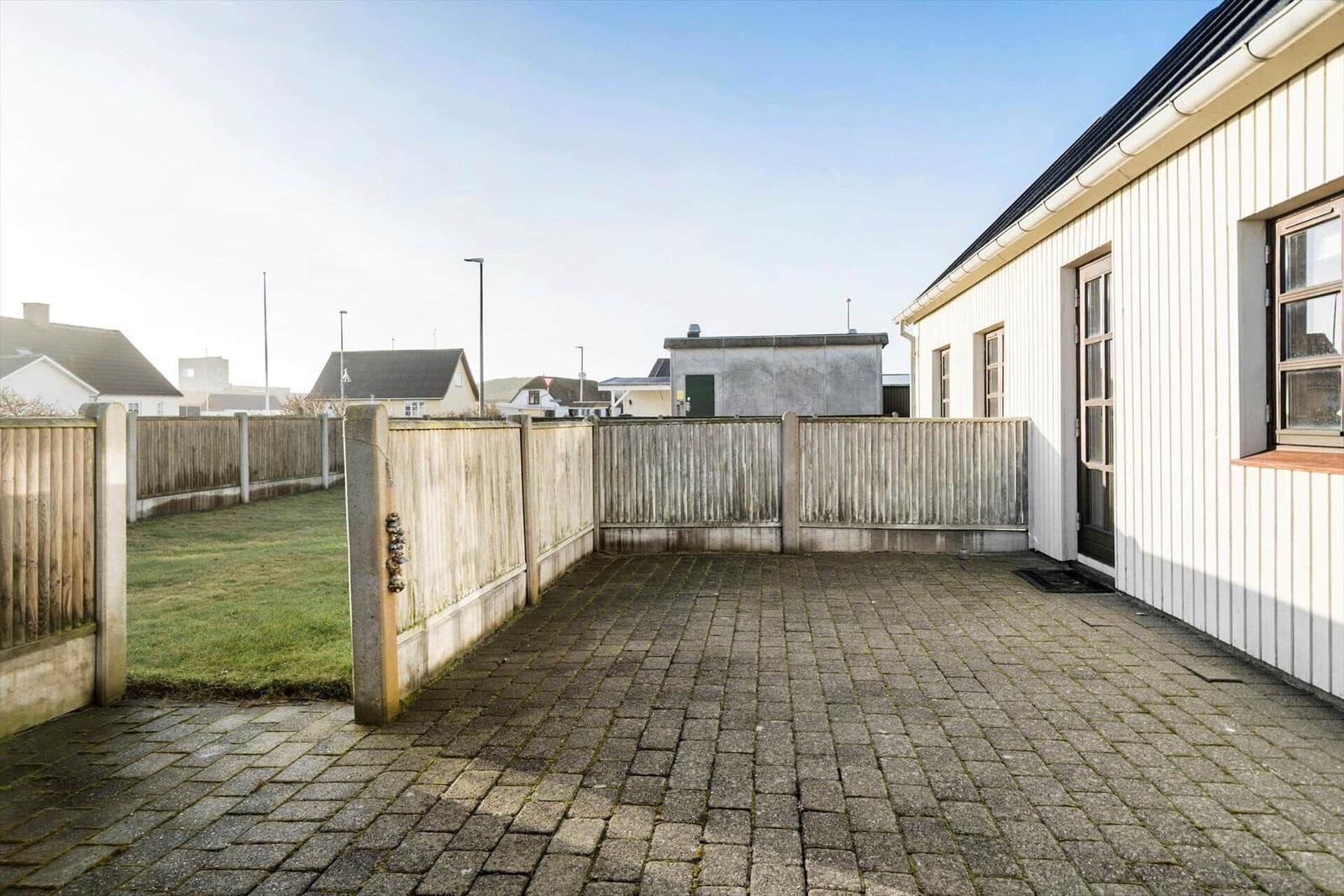 Backyard with paved area and wooden fence. Grass area beside the house.
