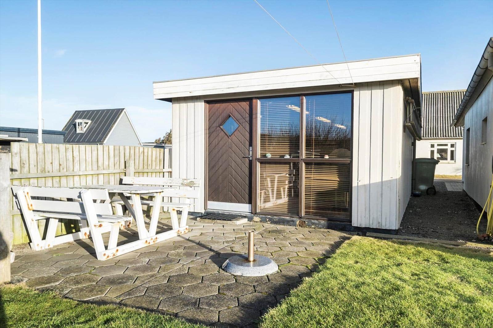 House with patio, white picnic table, wooden door, and windows with blinds.
