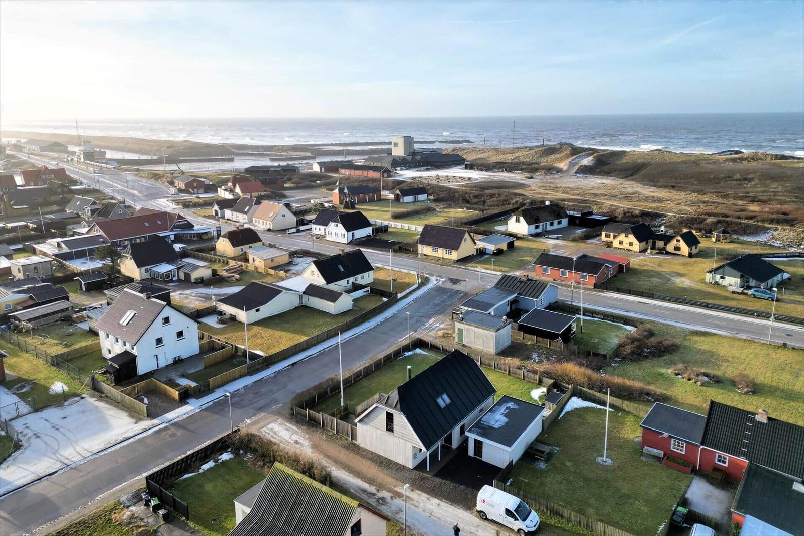 Aerial view of coastal village with houses, roads, and ocean in background.