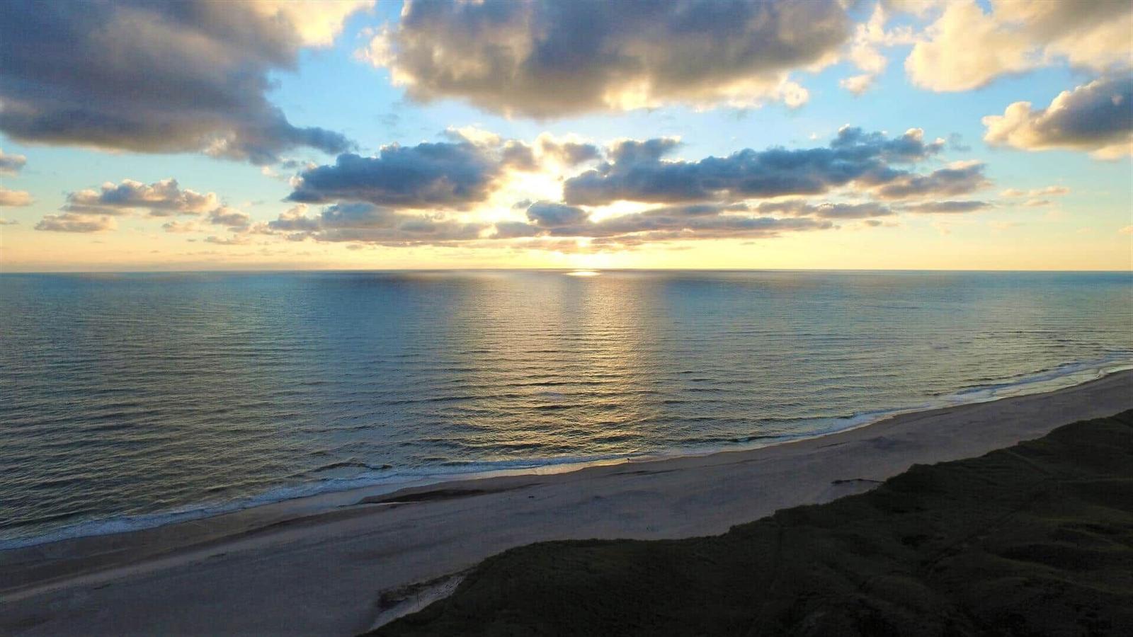 Sunset over sea and beach with clouds on the horizon.