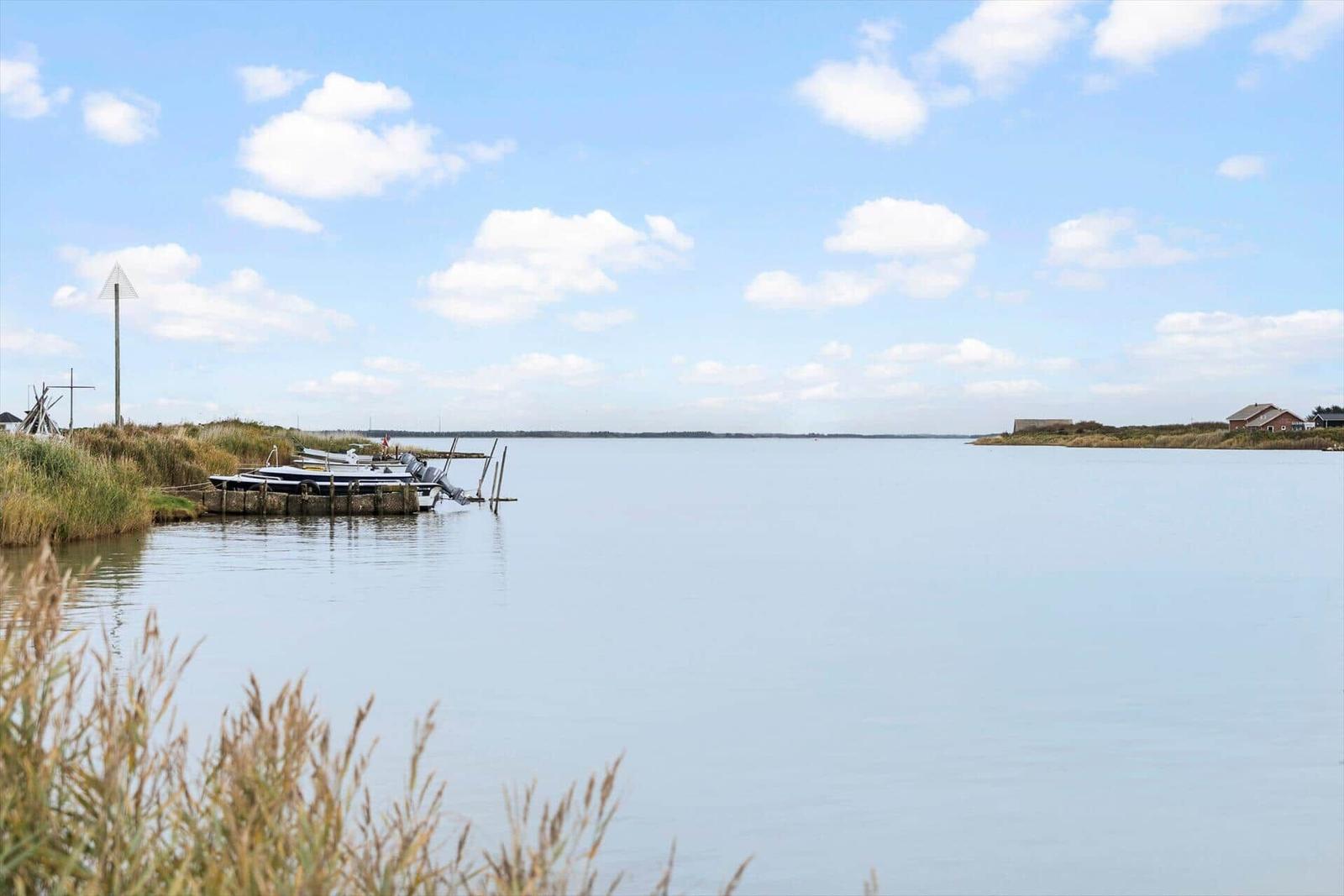 Boat is moored at the edge of a lake under a blue sky with white clouds.