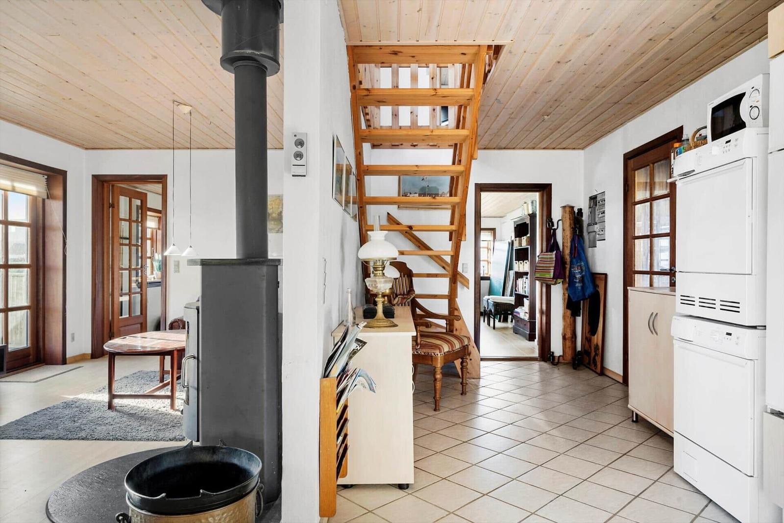 Kitchen with white appliances, wooden staircase, and wood stove inside.
