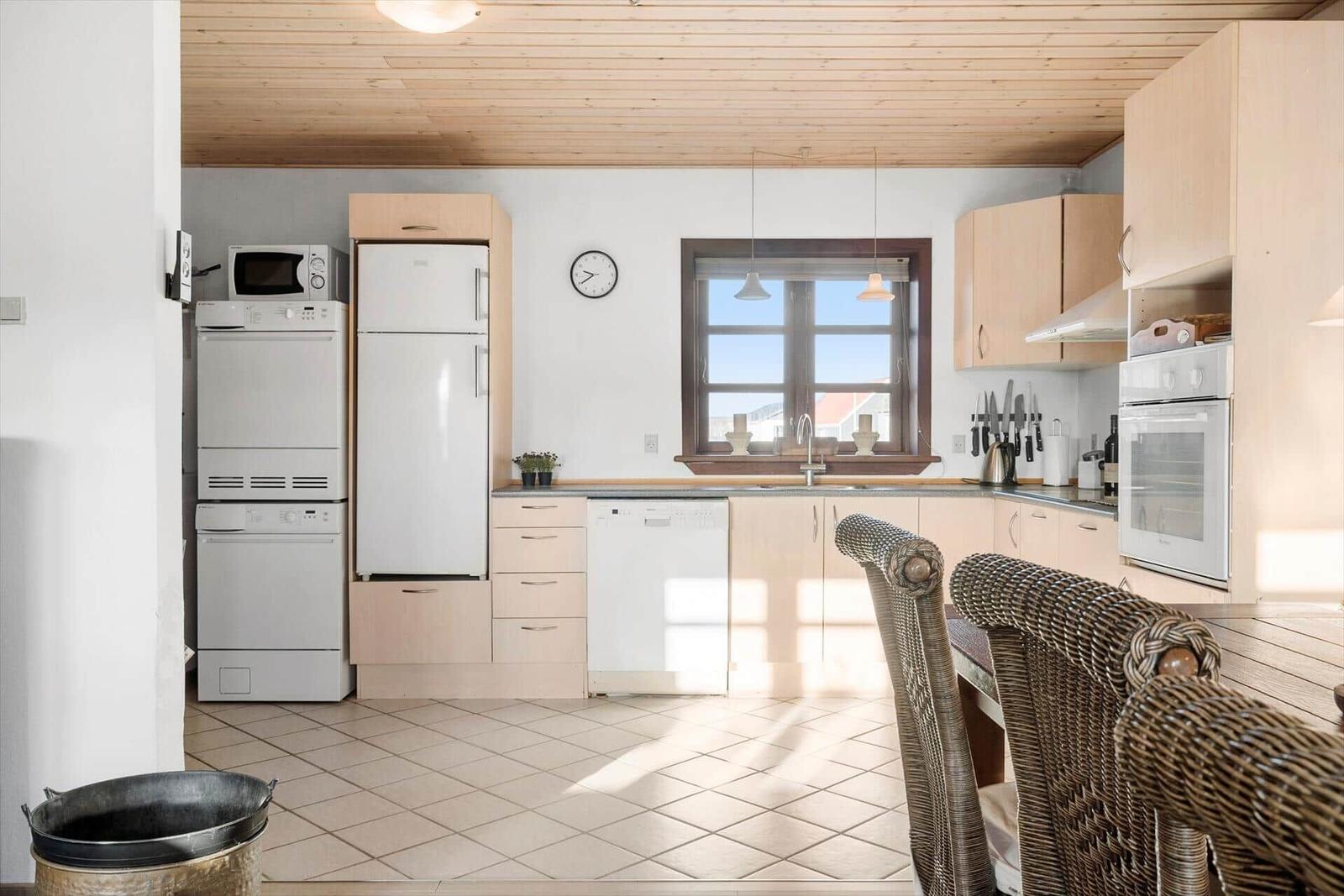 Kitchen with wooden ceiling, white appliances, and dining area with wicker chairs.