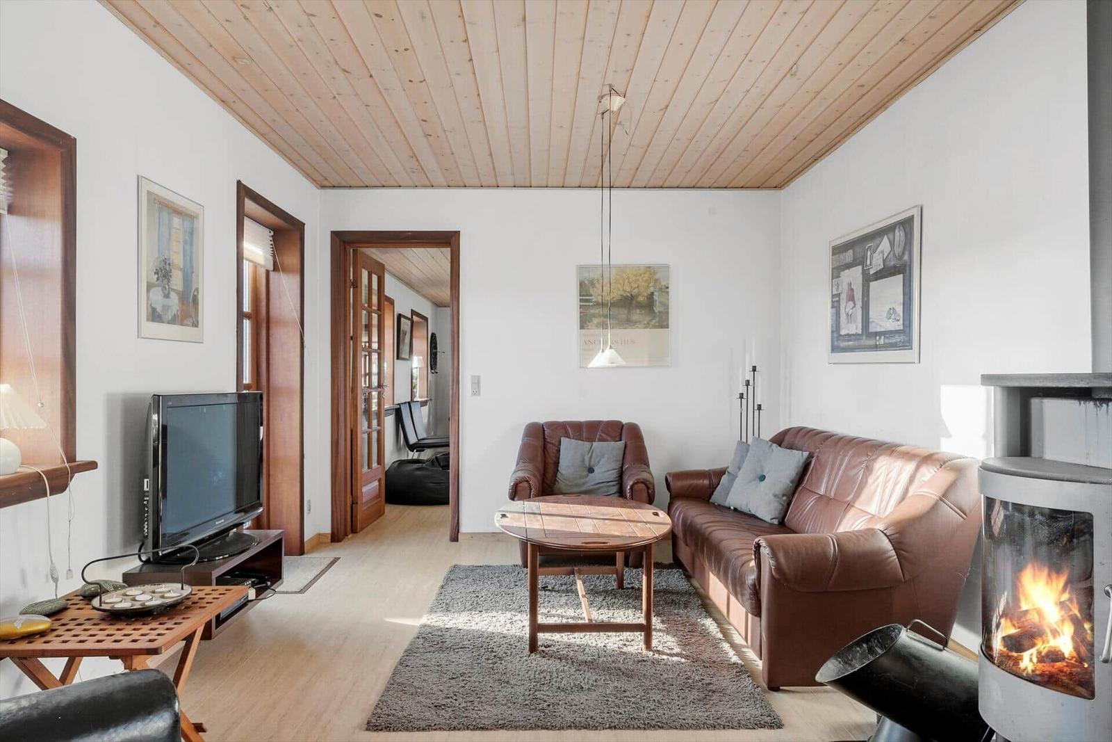 Living room with brown leather sofa, fireplace, and wooden ceiling. TV and table are present.