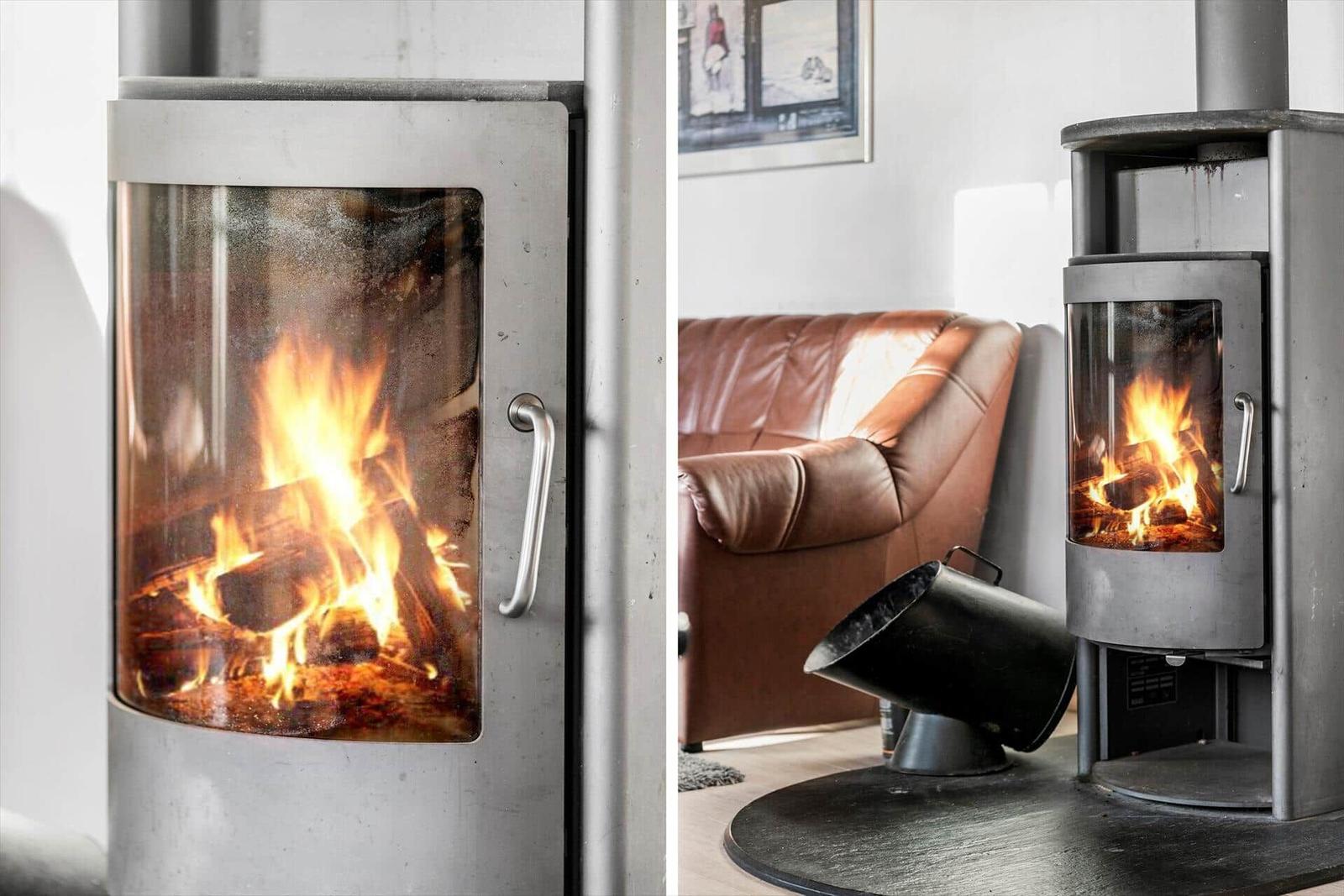 Modern wood stove with burning logs, next to a brown leather sofa.