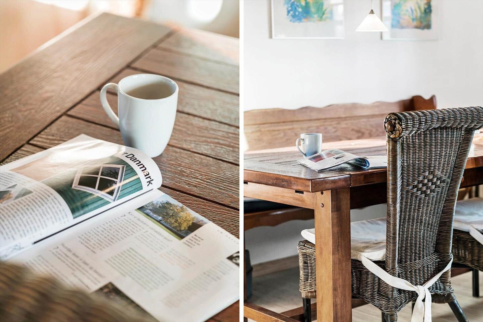 Wooden table with mug and newspaper. Rattan chair and wooden bench in background.