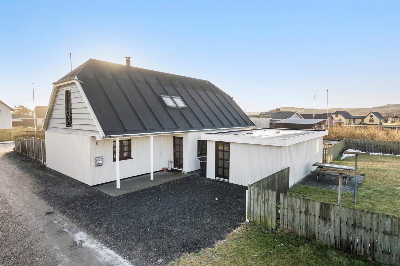 House with black roof and white siding, surrounded by lawn and fence.