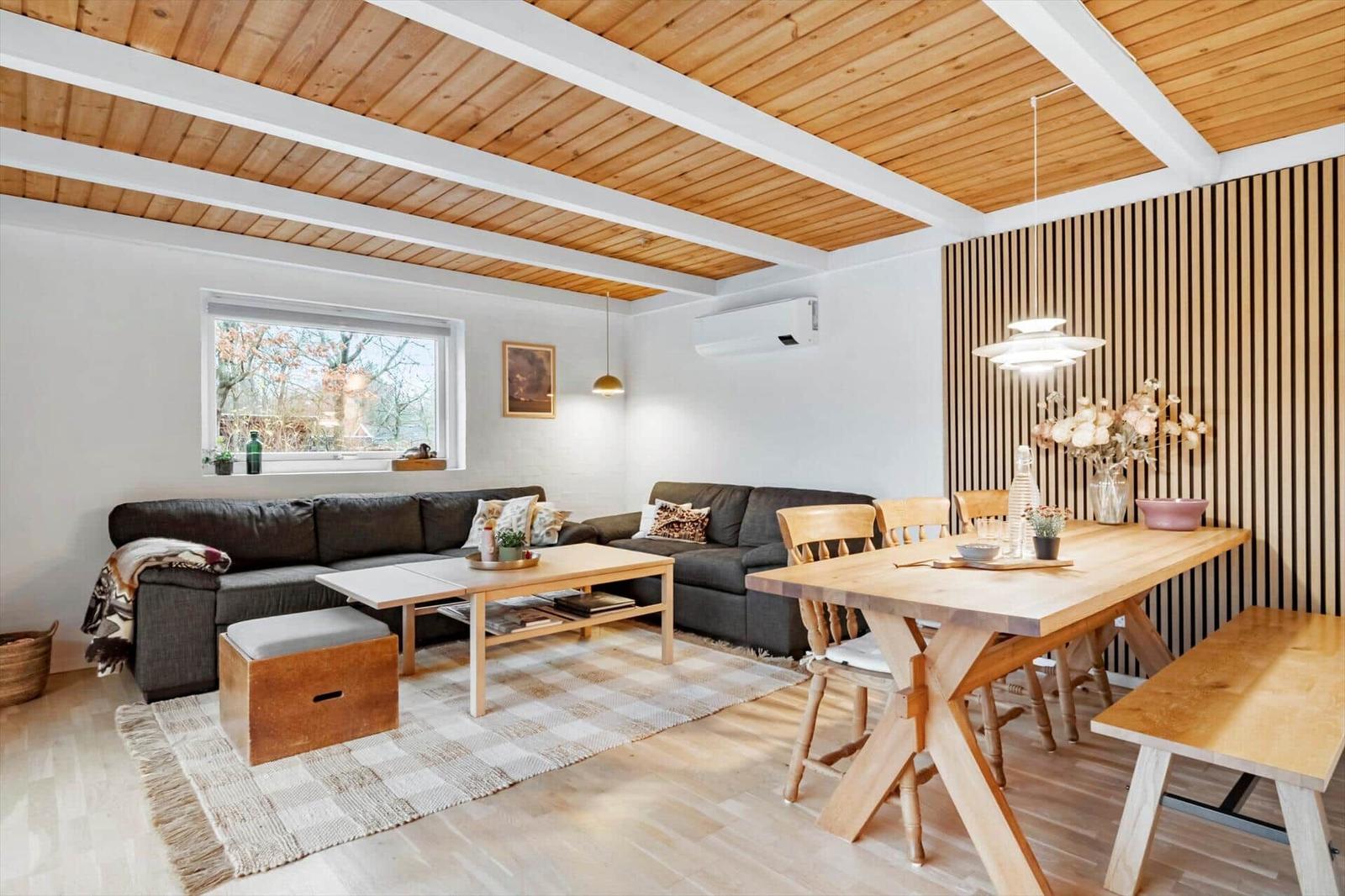 Wohn- und Essbereich mit Holzdecke, Sofa, Esstisch und Sitzbank.