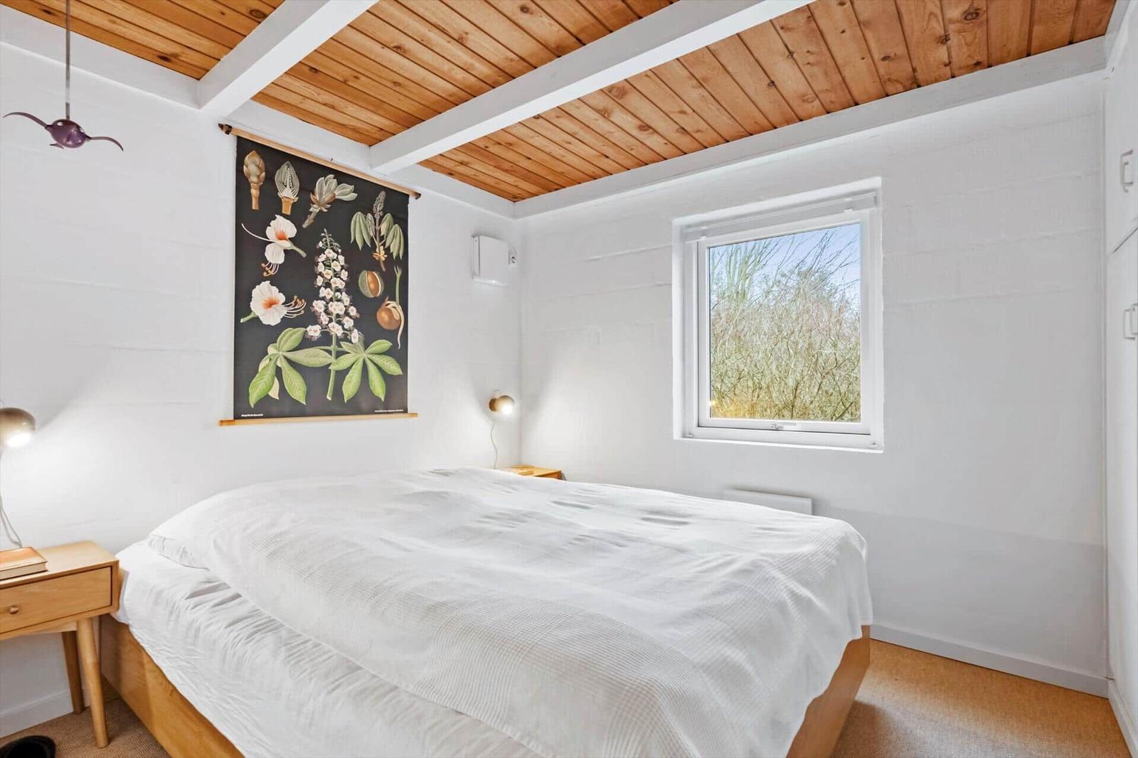 Schlafzimmer mit Bett, Holzdecke und Fenster. Wandbild und Nachttische.