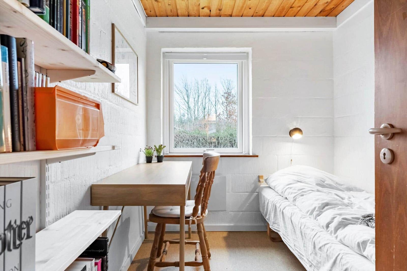 Ein Schlafzimmer mit Bett, Schreibtisch, Stuhl und Fenster. An der Wand hängen Bücherregale.