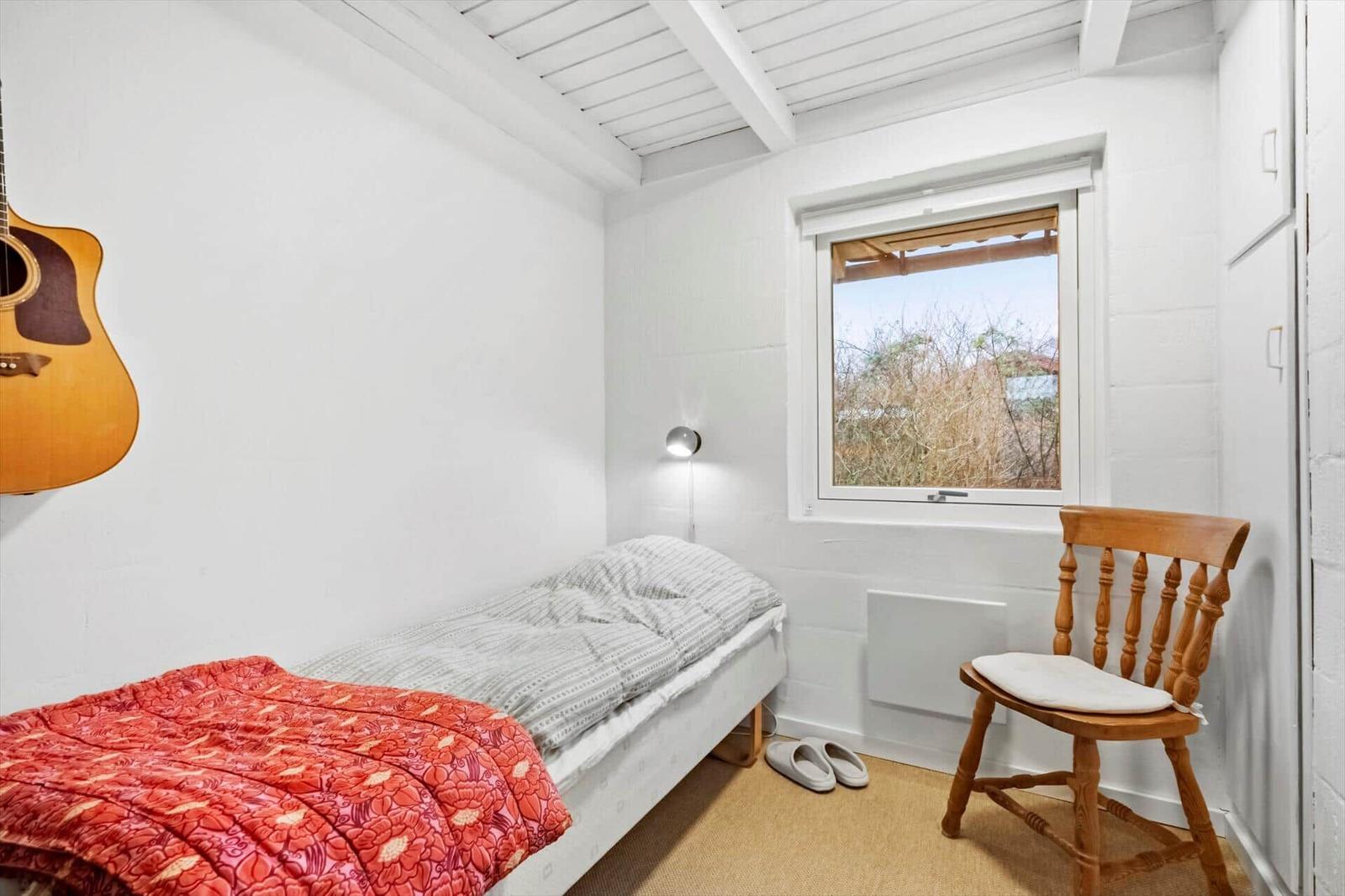 Ein Schlafzimmer mit einem Bett, einem Stuhl und einem Fenster. Eine Akustikgitarre hängt an der Wand.
