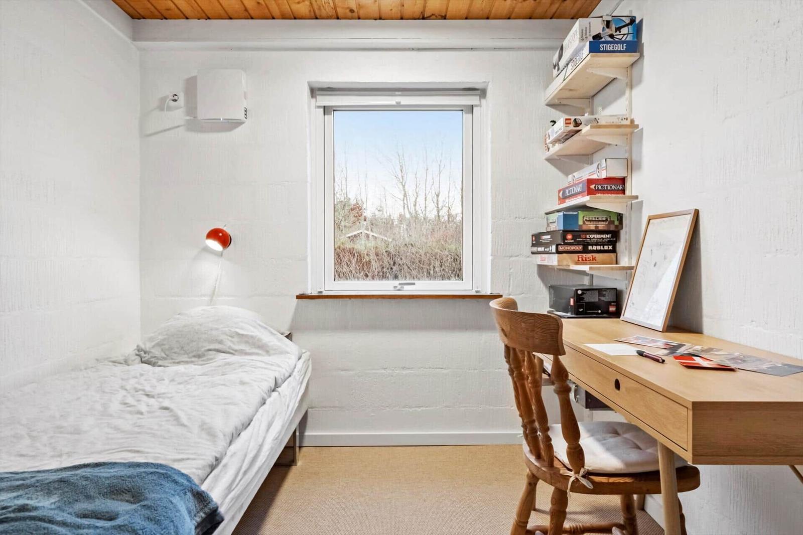 Ein Zimmer mit Bett, Schreibtisch und Fenster. An der Wand hängt eine Lampe.