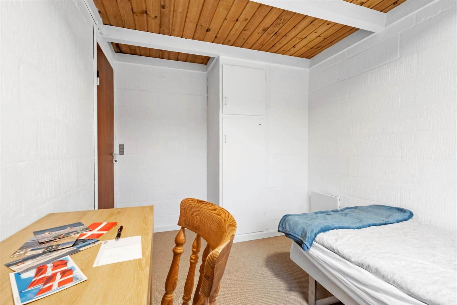 Ein Schlafzimmer mit einem Bett, einem Schreibtisch und einer Holztür.