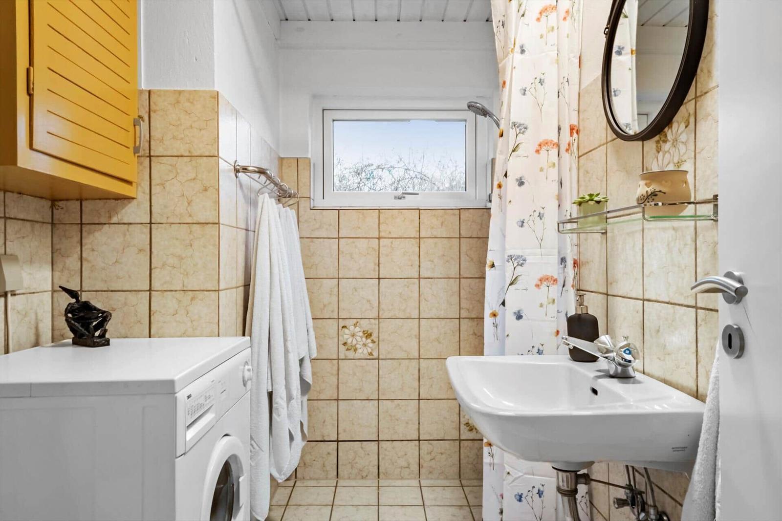 Badezimmer mit Waschmaschine, Spiegel und Duschvorhang mit Blumenmuster.