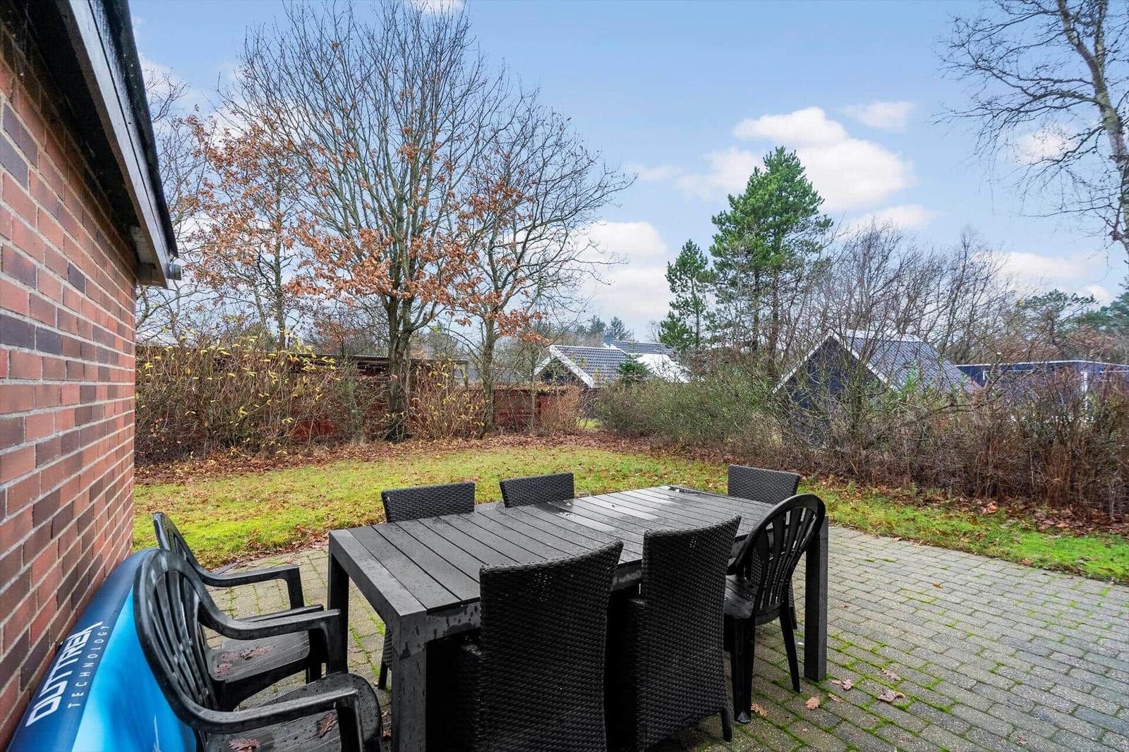 Terrasse mit Tisch und Stühlen, Garten und Bäume im Hintergrund.