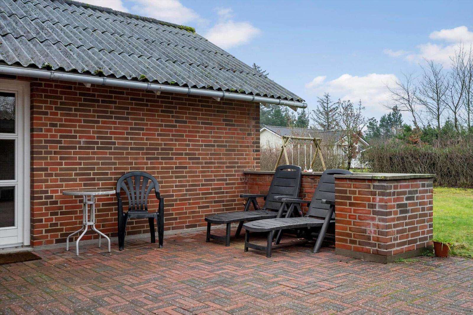 Terrasse mit zwei Liegestühlen, Tisch und Stuhl vor Backsteinhaus mit Garten.