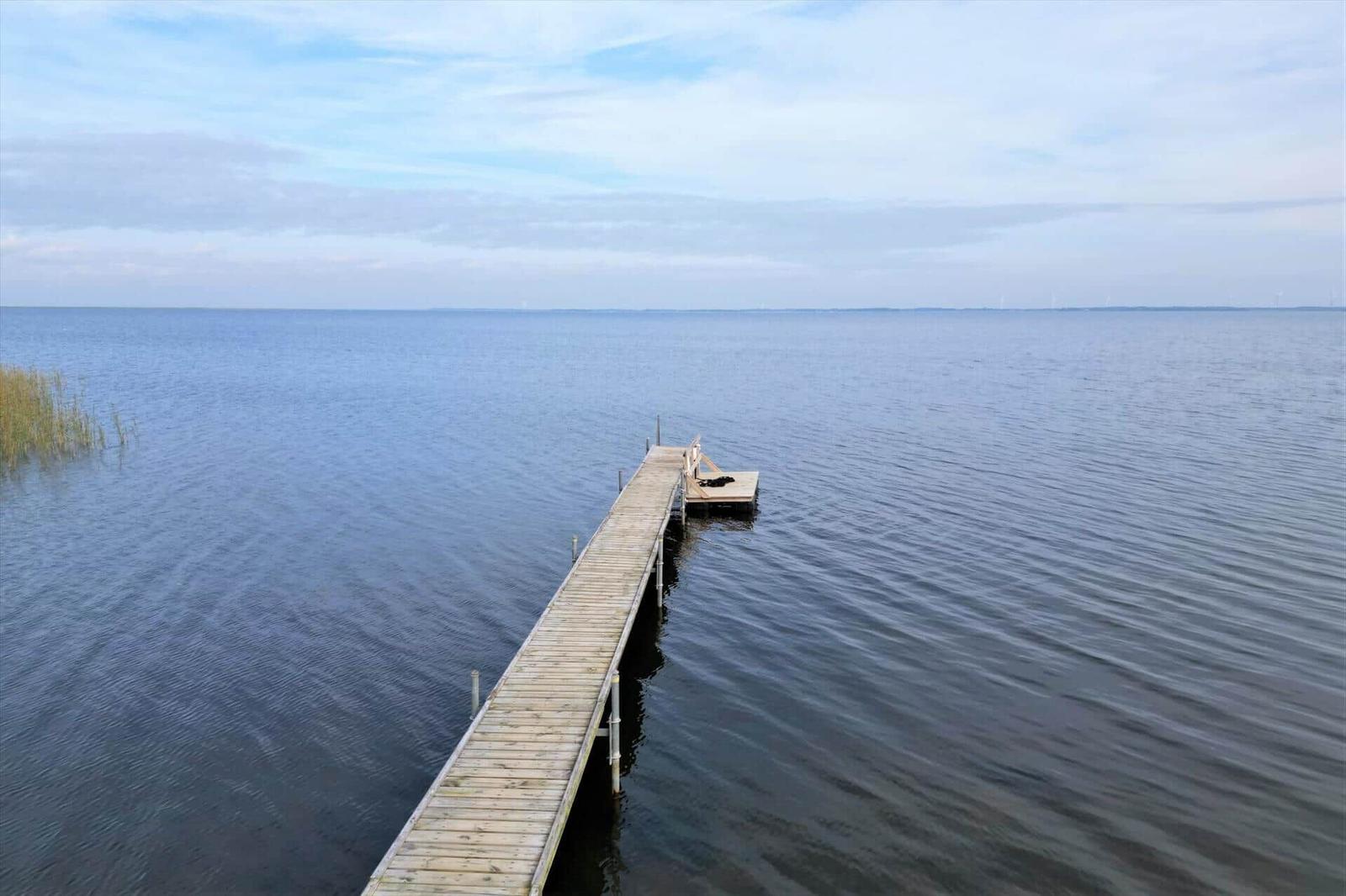 Holzsteg führt über ruhiges Wasser zu einer kleinen Plattform.