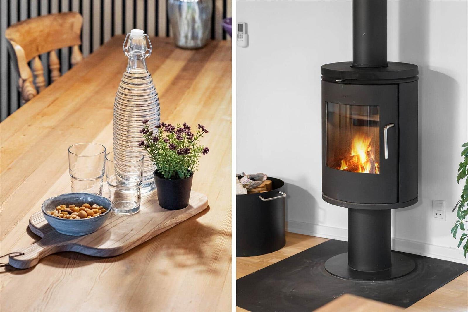 Holztisch mit Wasserglas, Nüssen und Pflanze. Kaminofen mit brennendem Feuer.