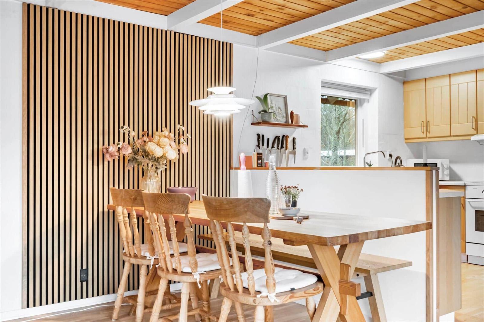 Essbereich mit Holztisch, Stühlen und Holzwand. Küche mit Küchenschränken und Fenster.