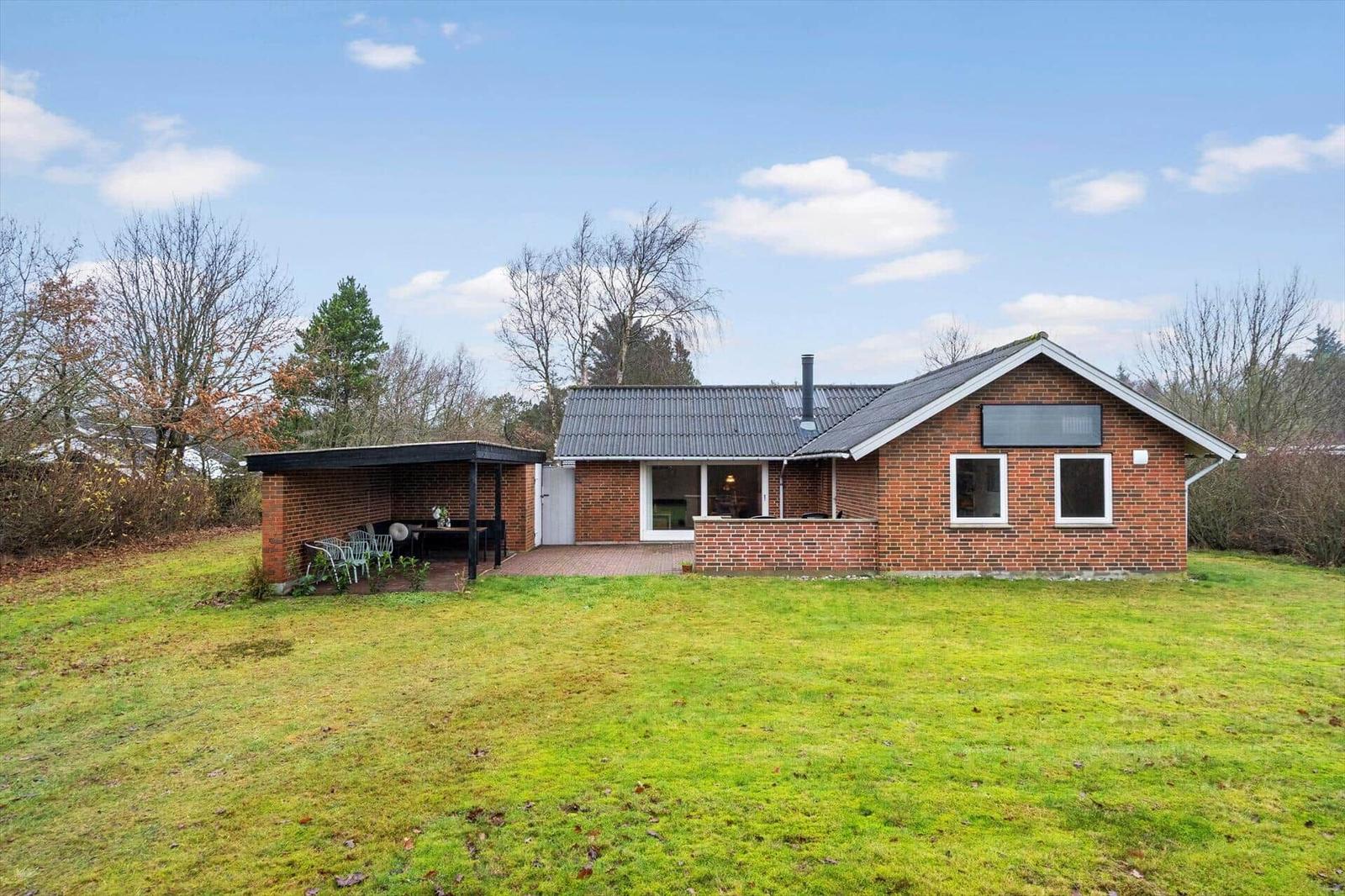 Ein Haus mit Backsteinfassade, großem Garten und überdachtem Sitzbereich.
