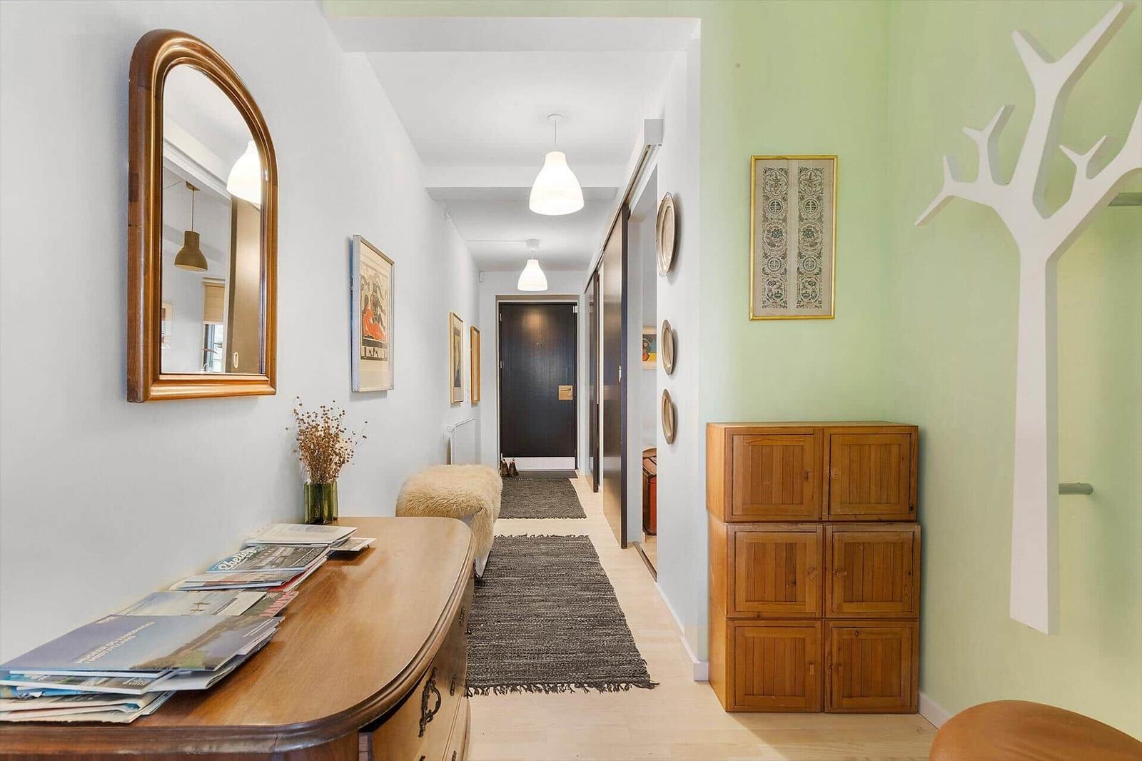 Hallway with wooden console, mirror, and wall decor. Wooden cabinet and rug visible.