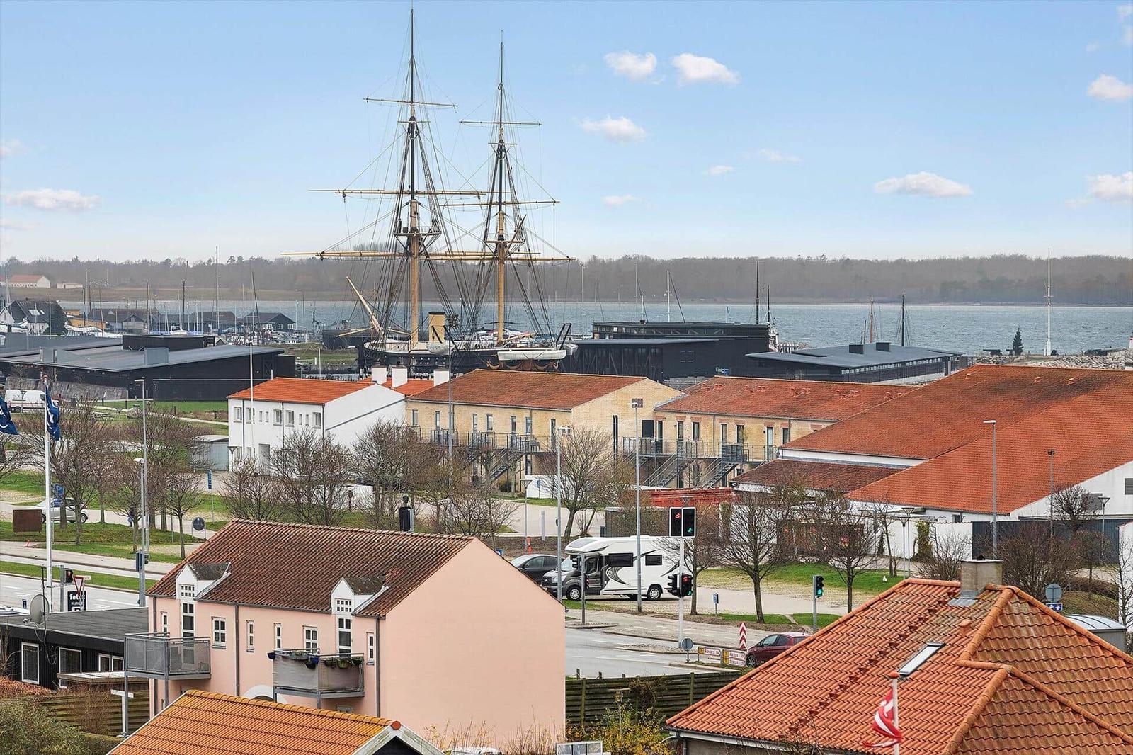 Harbor town with sailboat, red roofs, and water in the background.