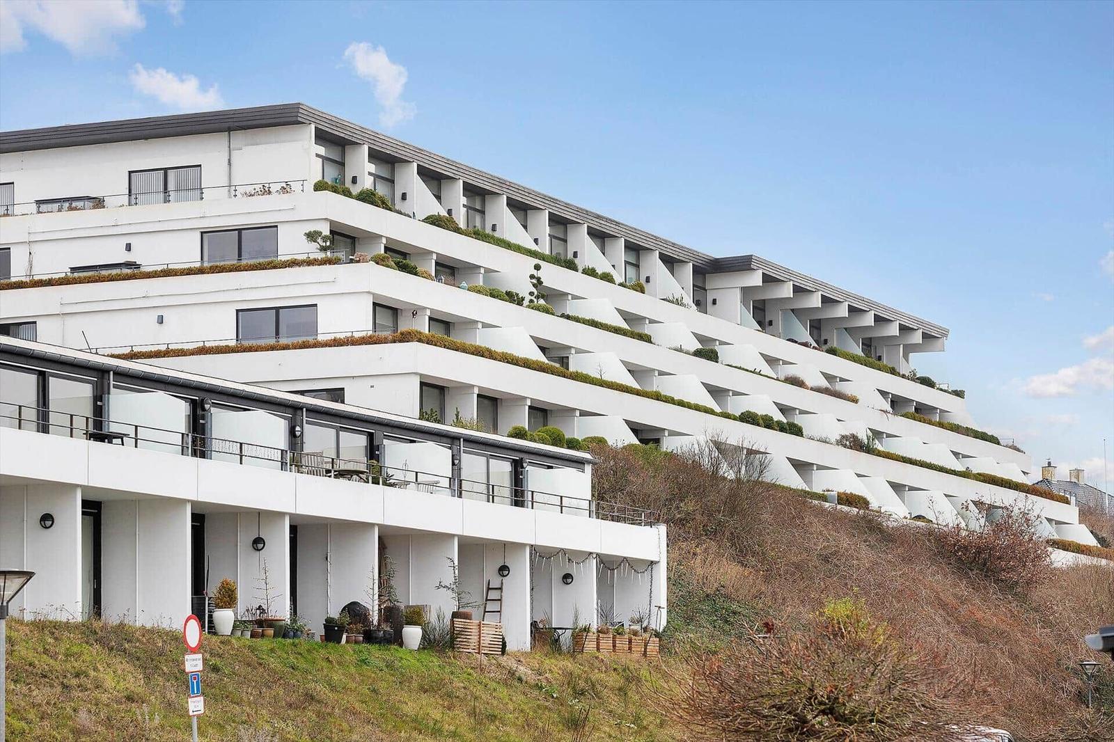 Modern multi-family house with terraces and green areas on a slope.