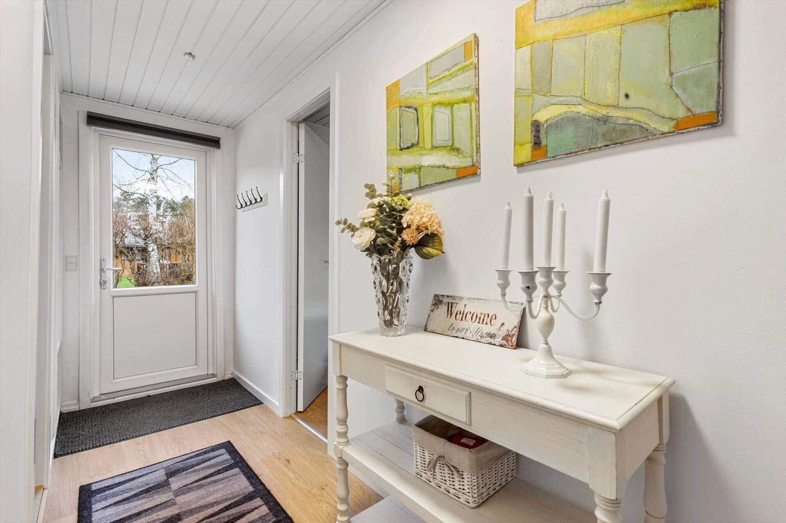 Entrance area with white walls, wooden floor, and a white table with vases and candles.