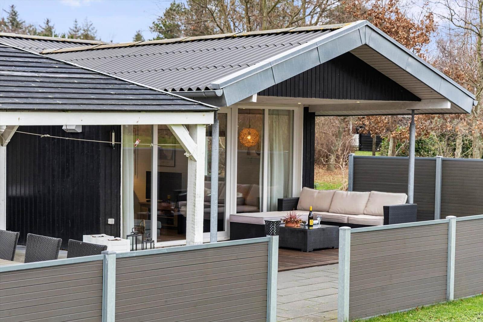 Terrace with sofa, table, and garden fence. Glass doors lead to the interior.
