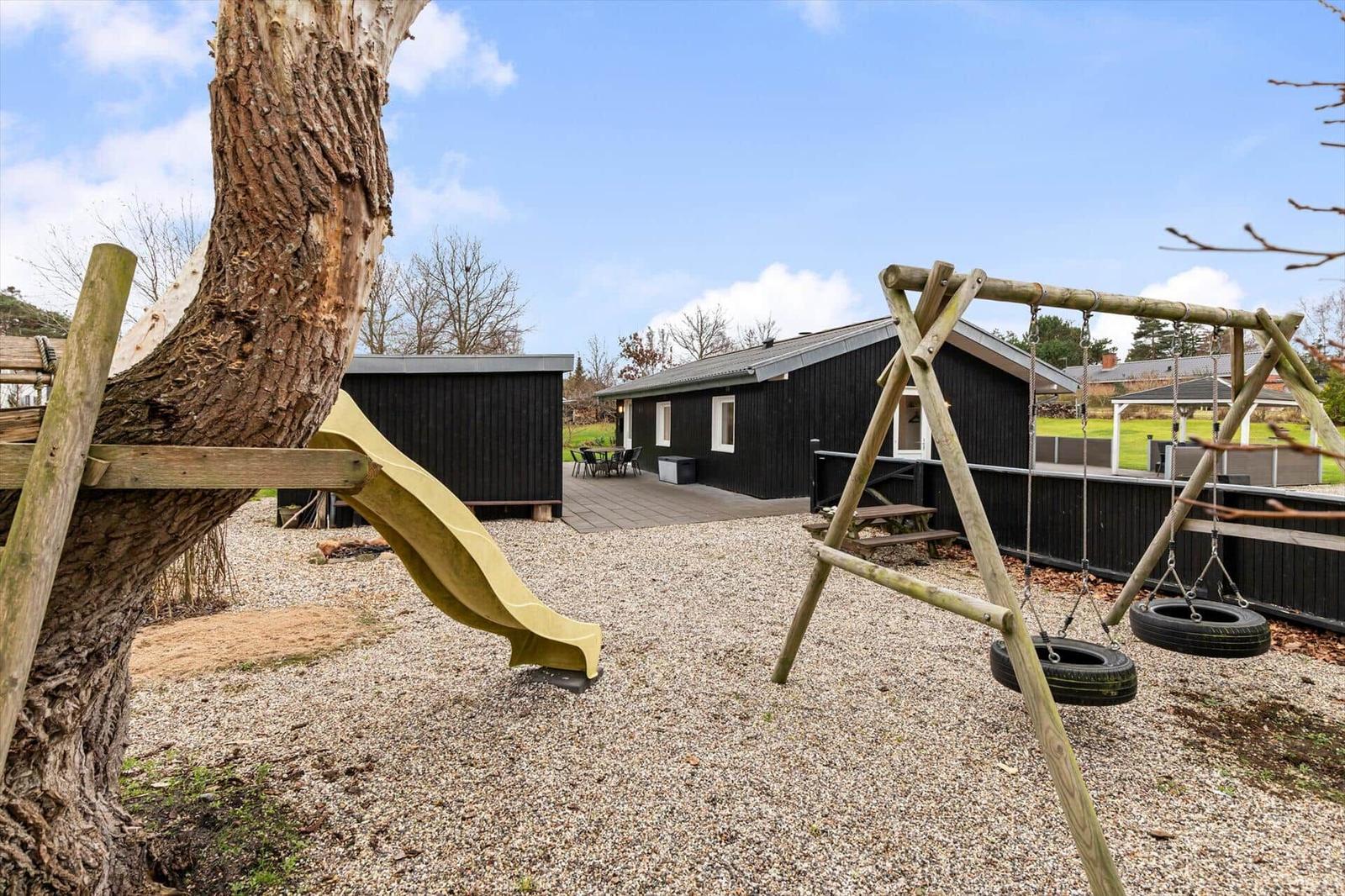 Backyard with playground, swing, and slide in front of a black house.