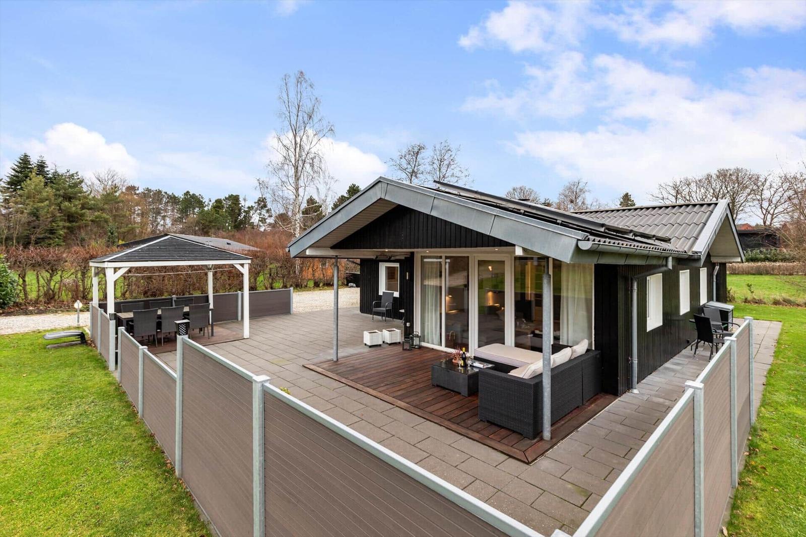 Modern villa with large outdoor area, terrace, and gazebo. Lawn and forest in the background.