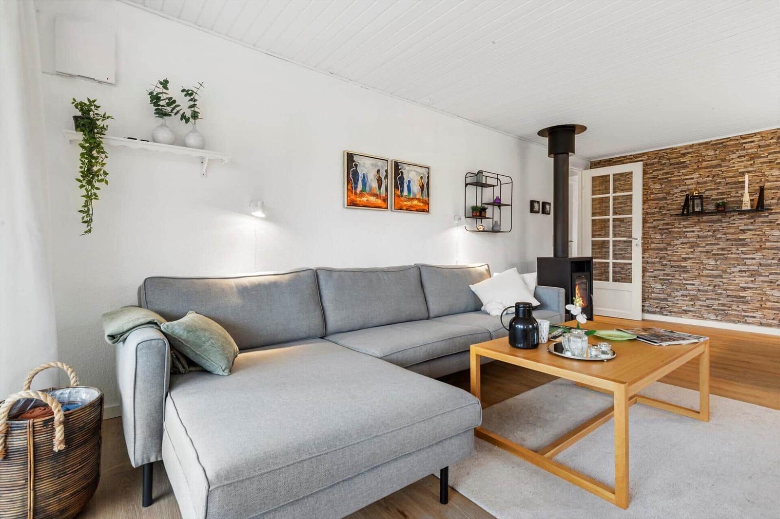 A living room with gray sofa, wooden table, and wood stove against stone wall.