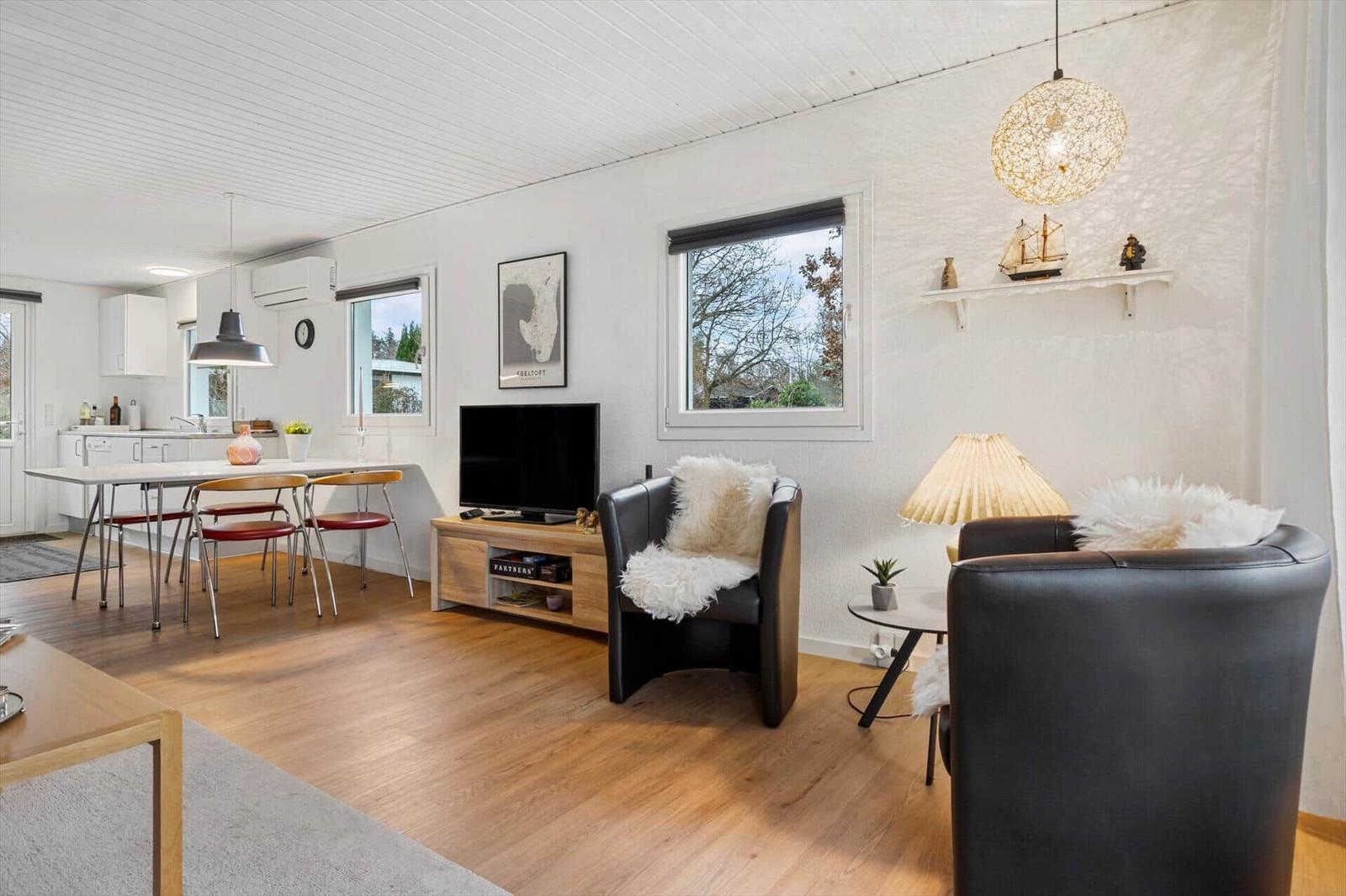 Living and dining area with TV, two armchairs, and kitchen area in background.