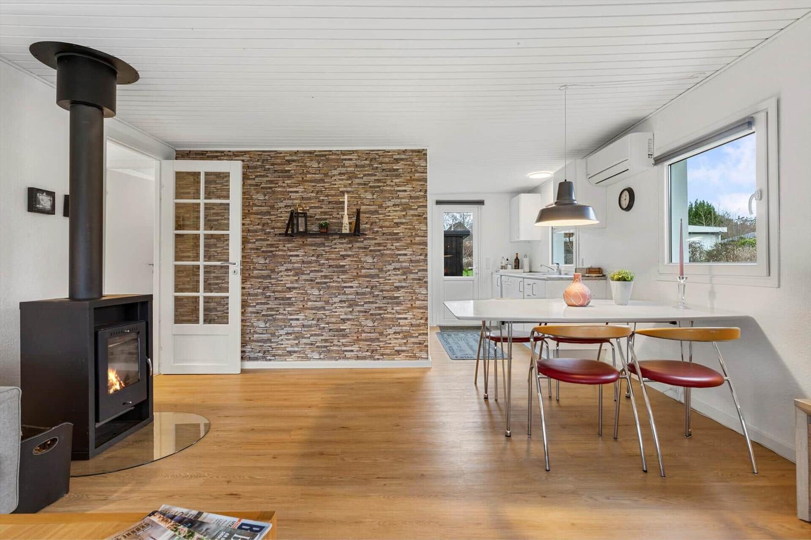 Living and dining area with fireplace, hardwood floor, and stone wall. Kitchen with dining table and window.