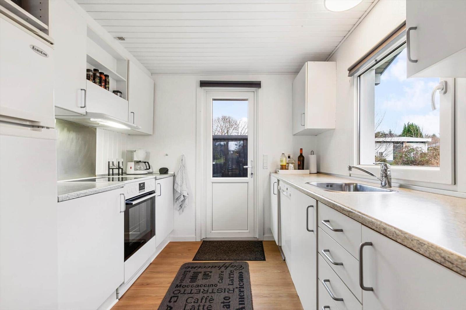 Kitchen with white cabinets, countertop, and window. Door leads outside.