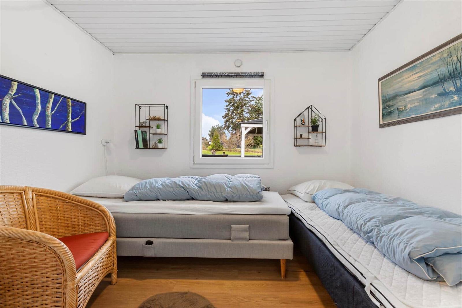 Two beds and a chair in the bedroom with garden view through window.