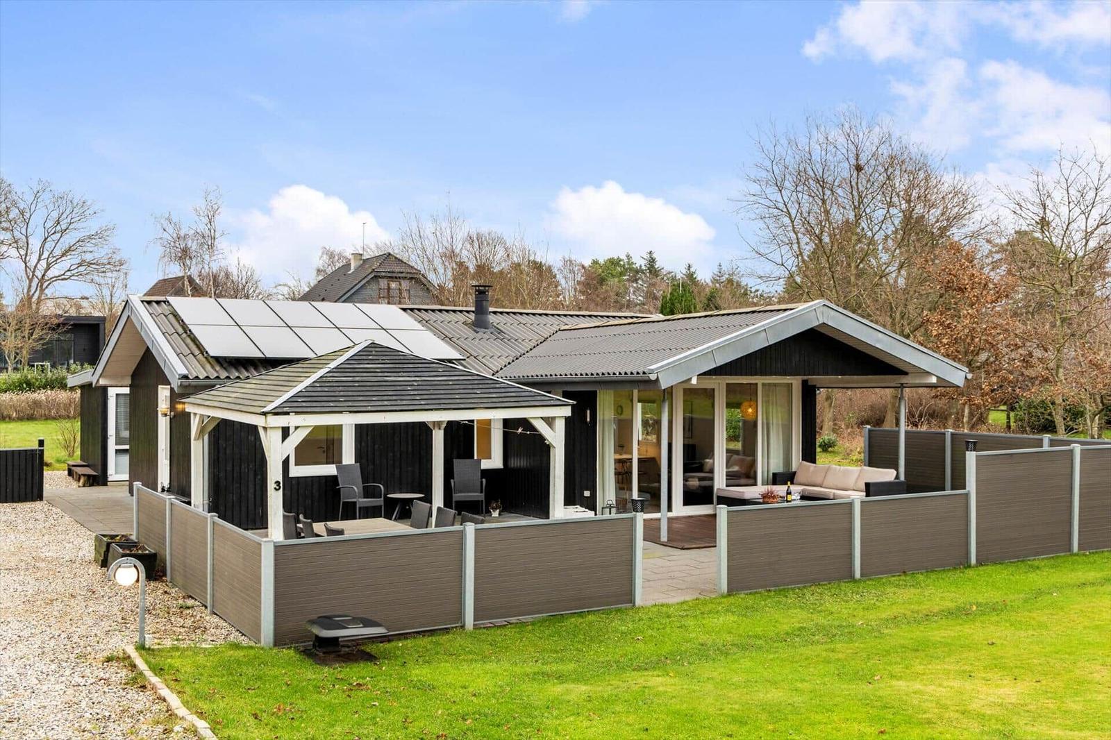 Modern holiday home with terrace, garden, and solar panels. Living area with seating.